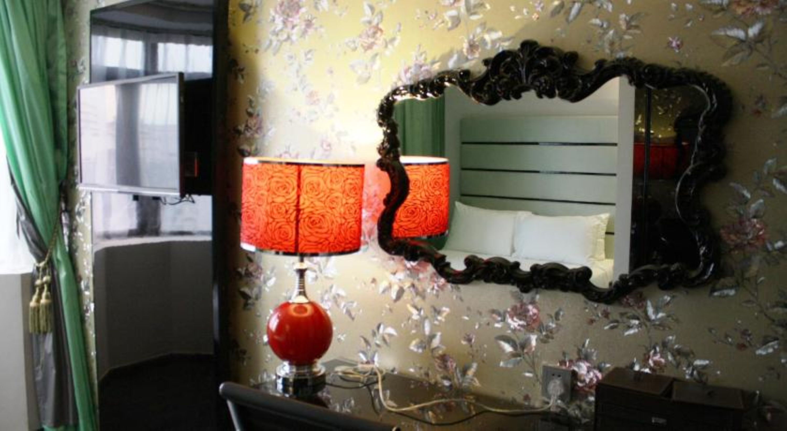 A room with a mirror, a lamp, and floral wallpaper.