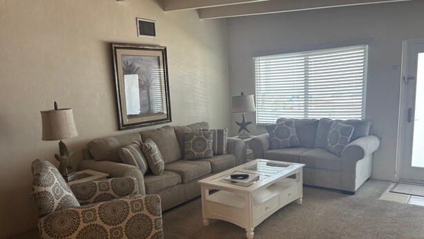 A living room with a sofa, armchair, coffee table, and a framed picture on the wall. - SR-12 Gulf Front 2/1 (Siesta Key)