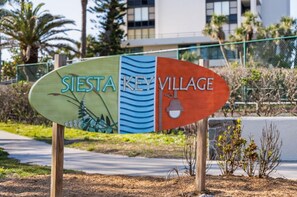 Schild für Sierra Key Village mit einem natürlichen Design auf einer Seite und einem modernen Gebäude im Hintergrund.