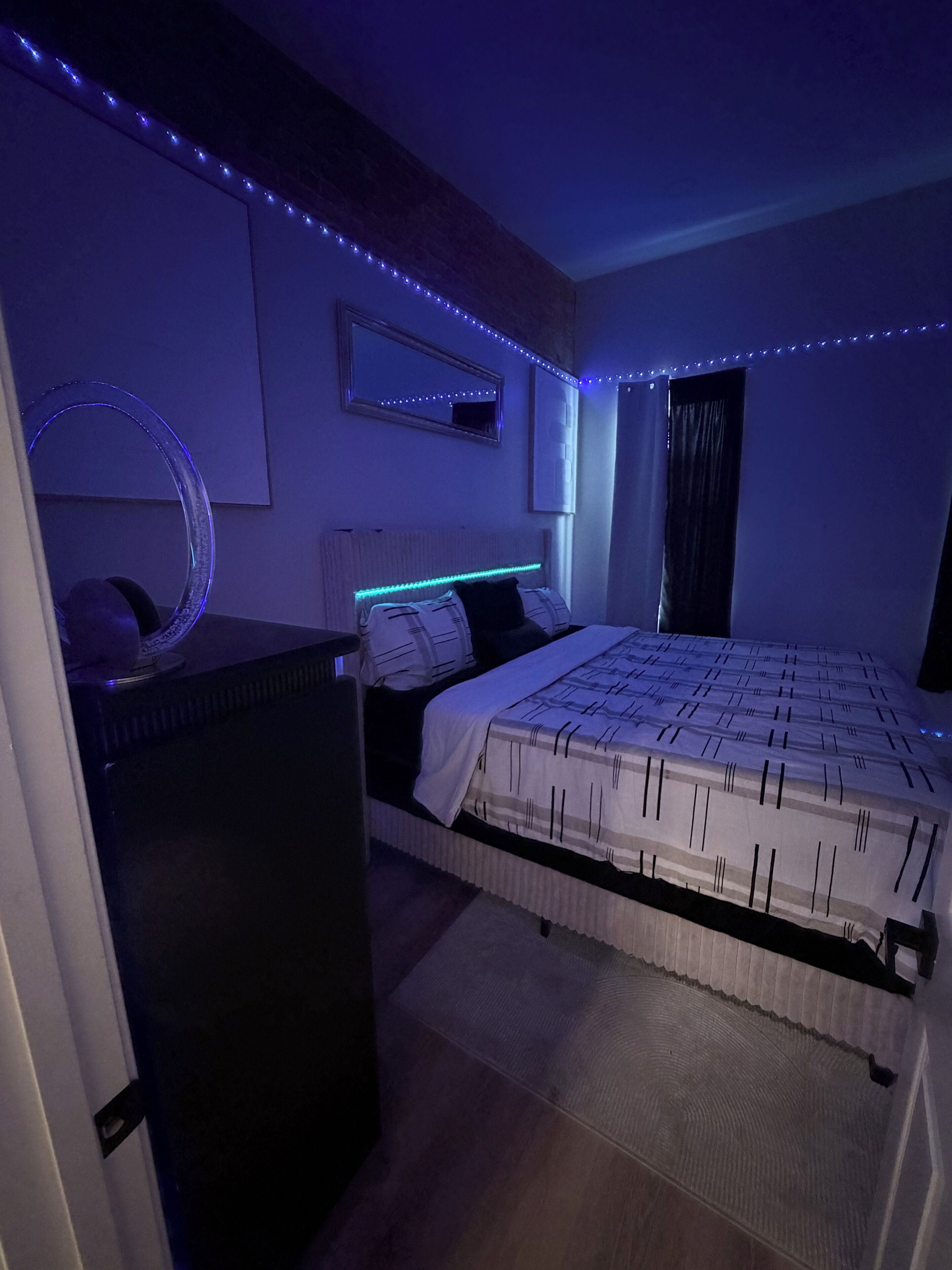 Et soveværelse med seng, kommode, spejl og LED-lys.