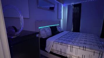 Et soveværelse med seng, kommode, spejl og LED-lys.