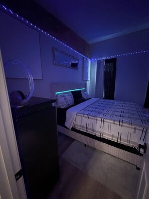 A bedroom with a bed, a dresser, a mirror, and LED strip lighting.