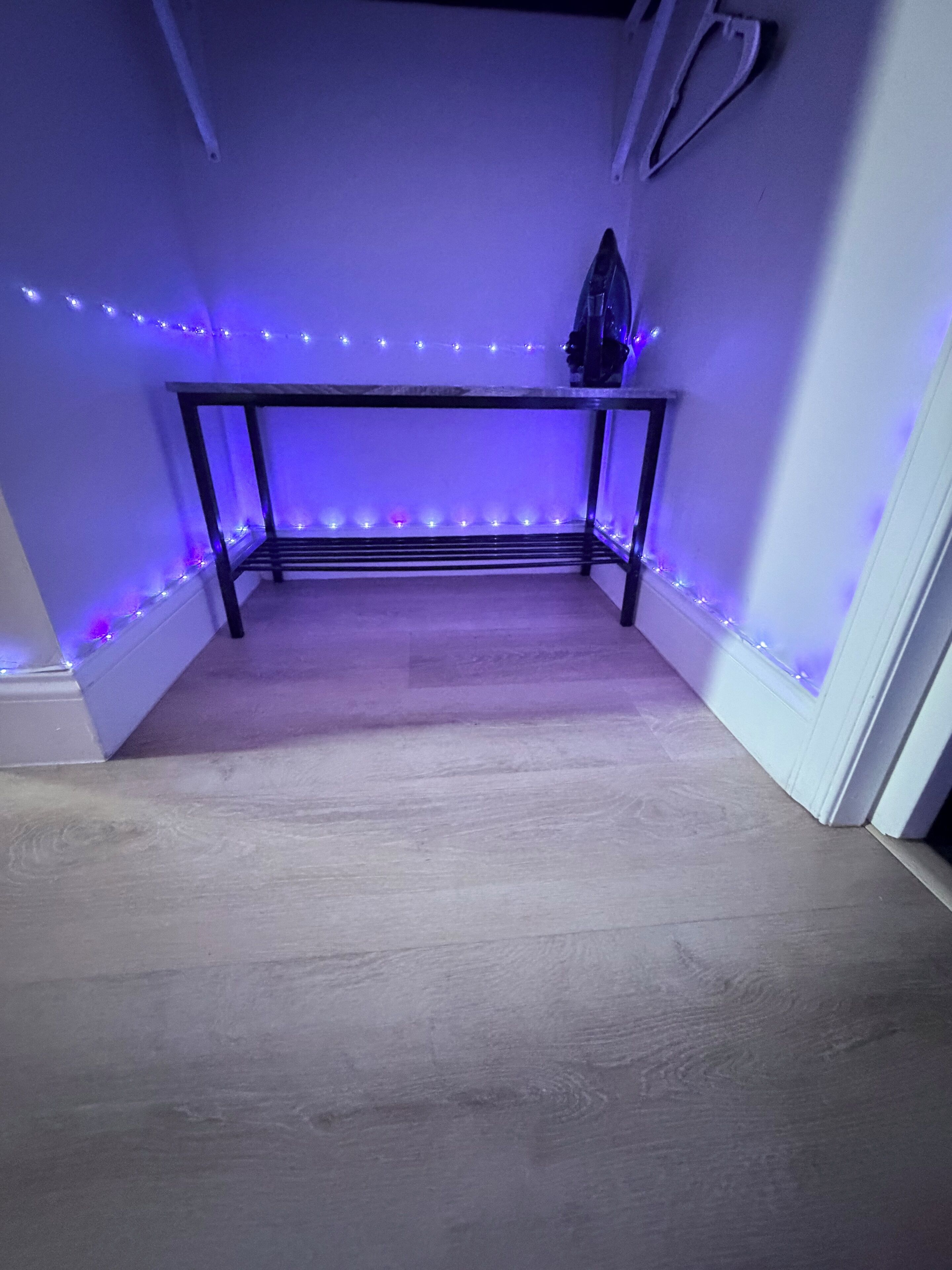 Una habitación con suelo de madera, una mesa de metal e iluminación de tiras LED moradas en el techo.