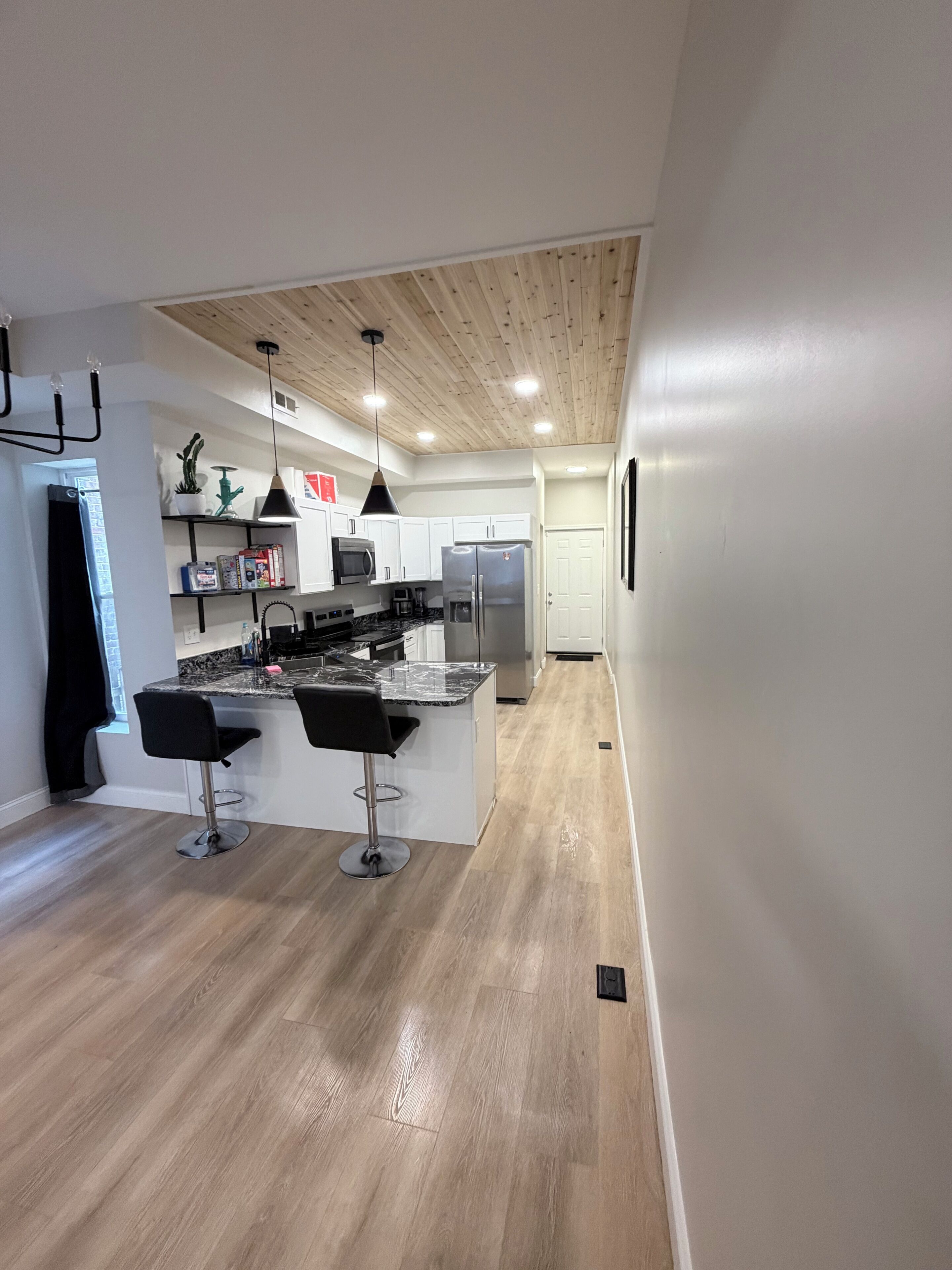 Una cocina moderna con una isla central, taburetes de bar y techo de madera.