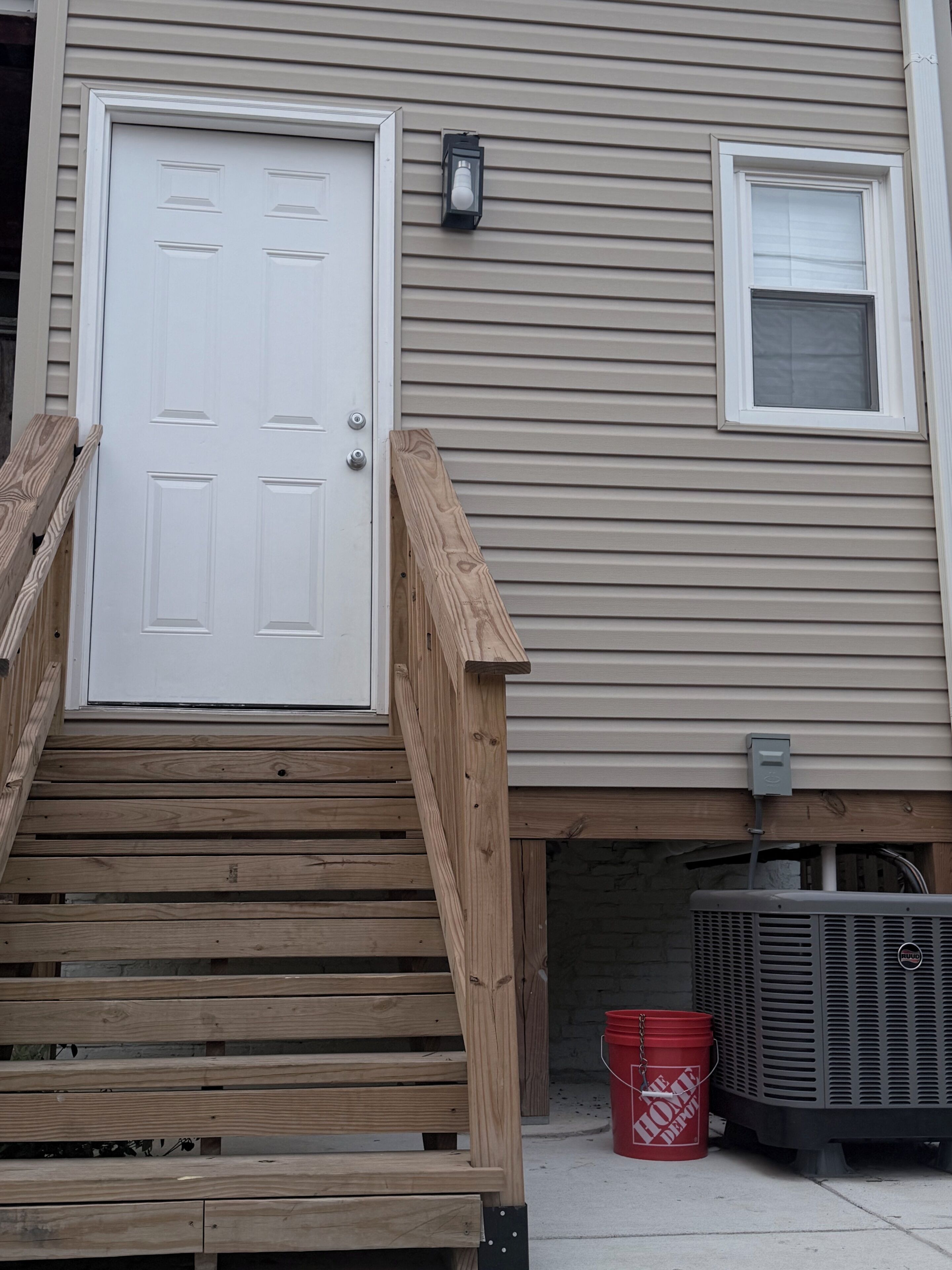 A residential building with a front door, a small window, and a wooden staircase leading to the entrance.