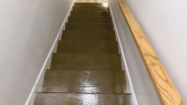 A staircase with wooden steps and a handrail, leading to a room with a black marble wall.