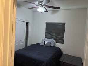 Ein Schlafzimmer mit einem Bett, einem Deckenventilator, einem Fenster mit Jalousien und einer Tür.