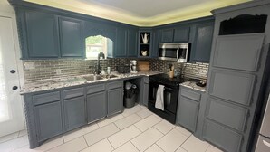 A kitchen with dark blue cabinets, a stainless steel microwave, and a granite countertop. -     Creekside Private Room & Bathroom  Fishing  Peaceful Retreat (Clute)