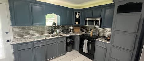 A kitchen with dark blue cabinets, a stainless steel microwave, and a granite countertop.