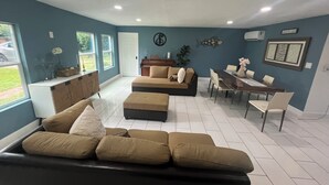 A living room with a sofa, dining table, and chairs. There is a window with a view of the outside. -     Creekside Private Room & Bathroom  Fishing  Peaceful Retreat (Clute)
