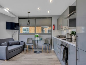 A modern kitchen with a built-in oven, a dining area with a glass table and chairs, and a grey sofa. - Hoxton Residence by Interhome (Hoxton)