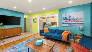 Ein modernes Wohnzimmer mit einer Couch, einem Couchtisch und einem Fernseher. Im Hintergrund ist eine Küchenzeile erkennbar.