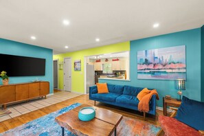 A modern living room with a sofa, coffee table, and a television. There is a kitchen area visible in the background. - 4-Bedroom Hot Tub Getaway Near Beaches & Wineries (Stevensville)