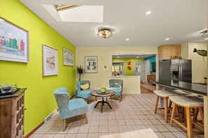 A modern kitchen with a dining area, featuring a large refrigerator, a dining table with chairs, and artwork on the walls. - 4-Bedroom Hot Tub Getaway Near Beaches & Wineries (Stevensville)