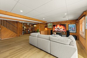 A spacious living area with a large sectional sofa, wooden flooring, a staircase, a bookshelf, and a fireplace. - 4-Bedroom Hot Tub Getaway Near Beaches & Wineries (Stevensville)