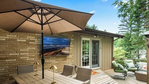 Eine Terrasse mit Tisch und Stühlen, ein an der Wand montierter Fernseher und eine Glastür zu einem überdachten Außenbereich.