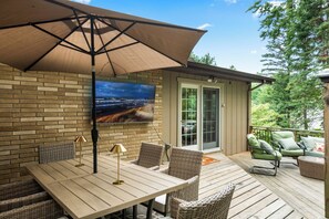 A deck with a table and chairs, a TV mounted on the wall, and a sliding glass door leading to a covered outdoor area. - 4-Bedroom Hot Tub Getaway Near Beaches & Wineries (Stevensville)