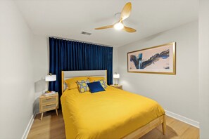 A bedroom with a bed, a ceiling fan, a nightstand with a lamp, and a framed picture on the wall. - 4-Bedroom Hot Tub Getaway Near Beaches & Wineries (Stevensville)