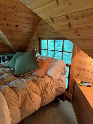 Une chambre à coucher avec un lit, des oreillers, une fenêtre et un plafond en bois.