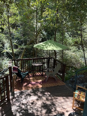 A wooden deck with a table and chairs, surrounded by dense forest. - Peaceful 1-bedroom studio cabin in enchanting Cazadero, a waterfall getaway (Cazadero)