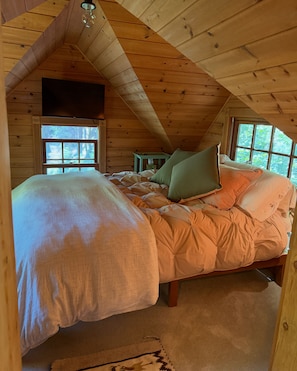 A cozy bedroom with a sloped ceiling, a bed with multiple pillows, a small table, and a window. - Peaceful 1-bedroom studio cabin in enchanting Cazadero, a waterfall getaway (Cazadero)