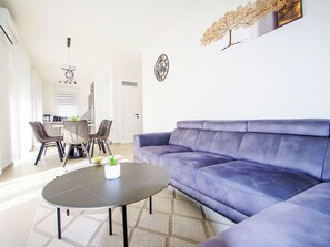 Een moderne woonkamer met een paarse bank, een ronde salontafel en een eethoek met stoelen en een tafel.
