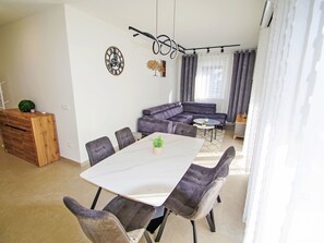 A modern living room with a sectional sofa, a dining table with chairs, and a decorative clock on the wall. - Charming 3-Bedroom Riviera by Interhome (Nedescina)