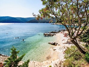 A coastal landscape with clear water, rocky shore, and a tree-lined beach. - Charming 3-Bedroom Riviera by Interhome (Nedescina)