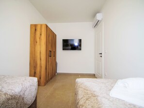 A bedroom with two beds, a wooden wardrobe, a television on the wall, and an air conditioning unit. - Charming 3-Bedroom Riviera by Interhome (Nedescina)