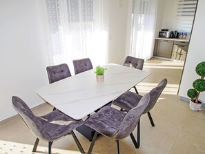 A modern dining area with a rectangular table, six upholstered chairs, and a potted plant. - Charming 3-Bedroom Riviera by Interhome (Nedescina)