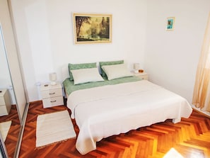 Ein Schlafzimmer mit Bett, Nachttischen, einem Spiegel, einem Bild an der Wand und Holzboden.