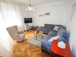 Moderni olohuone, jossa on sohva, nojatuoli, sohvapöytä ja televisio, joka on sijoitettu jalustalle.