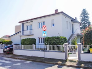Ein zweigeschossiges Gebäude mit weißer Fassade und einem Balkon im oberen Stockwerk, sowie ein Verbotsschild für Parkplätze.