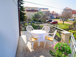 Un balcon avec une table ronde et des chaises, un petit jardin agrémenté de fleurs et une vue sur le quartier.
