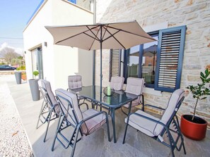 Een terras buiten met een glazen tafel, vier stoelen, een grote parasol en een potplant.