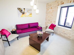A living room with a purple sofa, two white chairs, a coffee table, and a stone wall. - Stara Hiža by Interhome (Valbandon)