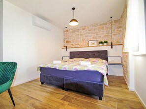 Quarto com cama, cadeira, parede de pedra e luminária pendente.