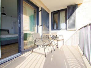 Ein Balkon mit Glastür zum Schlafzimmer, ein Tisch mit Stühlen und Blick ins Freie.