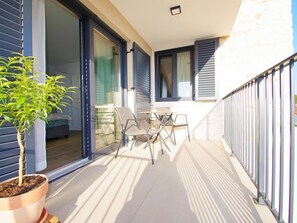 Ein Balkon mit einem Blumentopf, einem Tisch mit Stühlen und Blick ins Innere des Gebäudes.