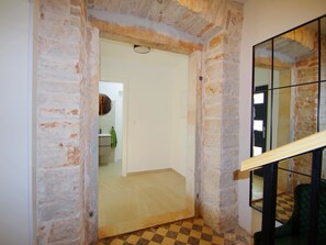 Quarto com paredes de tijolo aparente, piso de madeira e porta de vidro que dá para um banheiro.