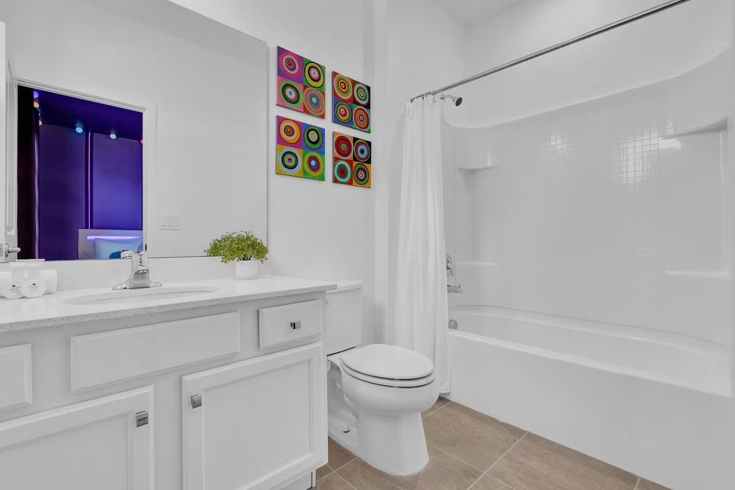 Une salle de bain moderne avec un lavabo, des toilettes et une baignoire, le tout de couleur blanche. Au-dessus du lavabo, on trouve des œuvres d'art murales colorées de forme circulaire.