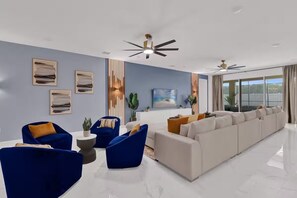 A modern living room with a sectional sofa, blue armchairs, and a ceiling fan. - 15BR Sonoma Resort Home in Kissimmee w/ Pool & Game Room (Kissimmee)