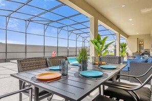 An outdoor dining area with a glass ceiling, metal-framed tables, and wicker chairs. - 15BR Sonoma Resort Home in Kissimmee w/ Pool & Game Room (Kissimmee)