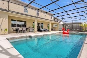 A swimming pool with a glass enclosure, outdoor seating, and a red flamingo float. - 15-Suite Luxury Villa | Sleeps 32 | Private Pool (Kissimmee)