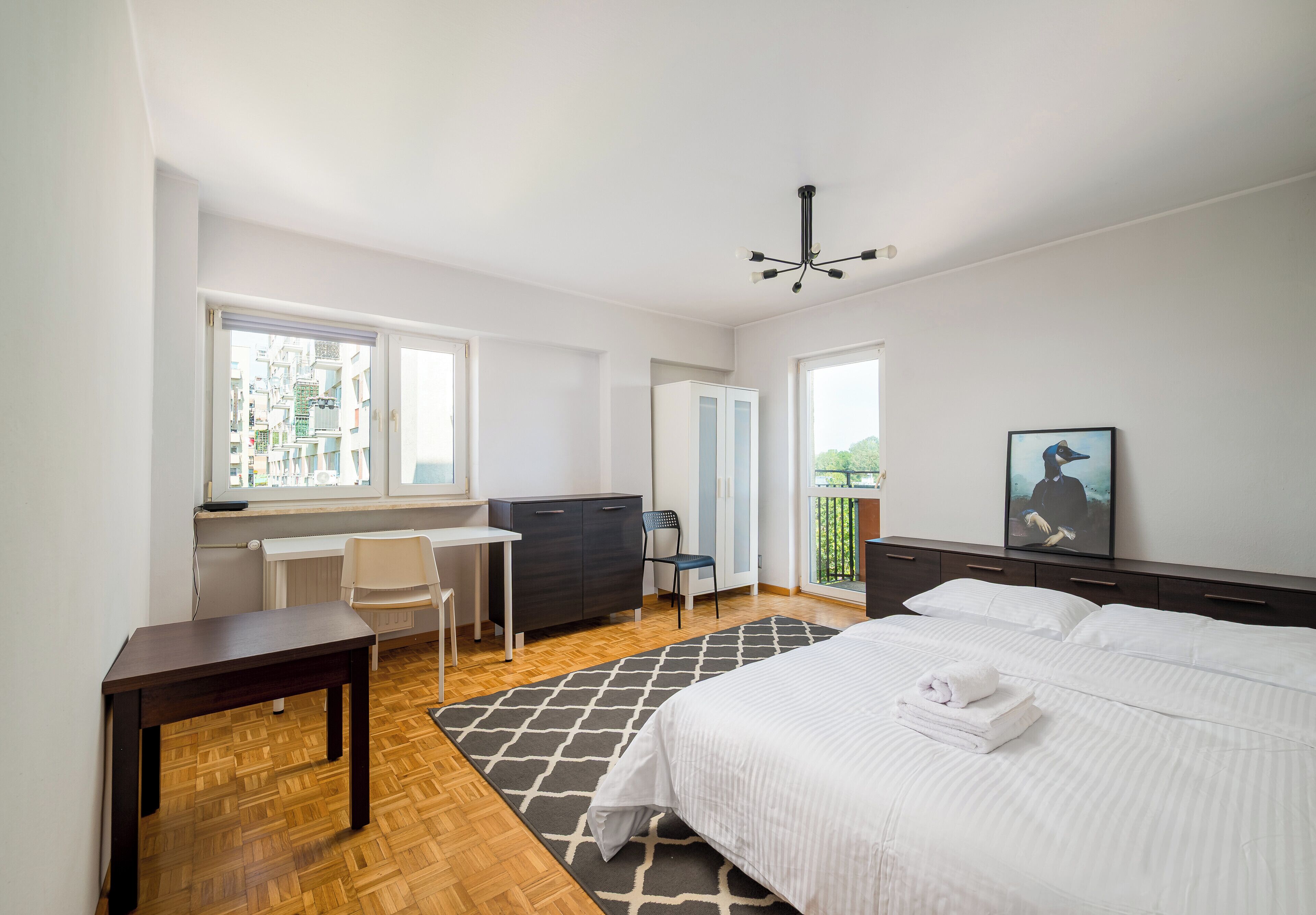Ein Hotelzimmer mit Bett, Schreibtisch, Stuhl, Heizkörper und einem Fenster mit Blick auf Gebäude.