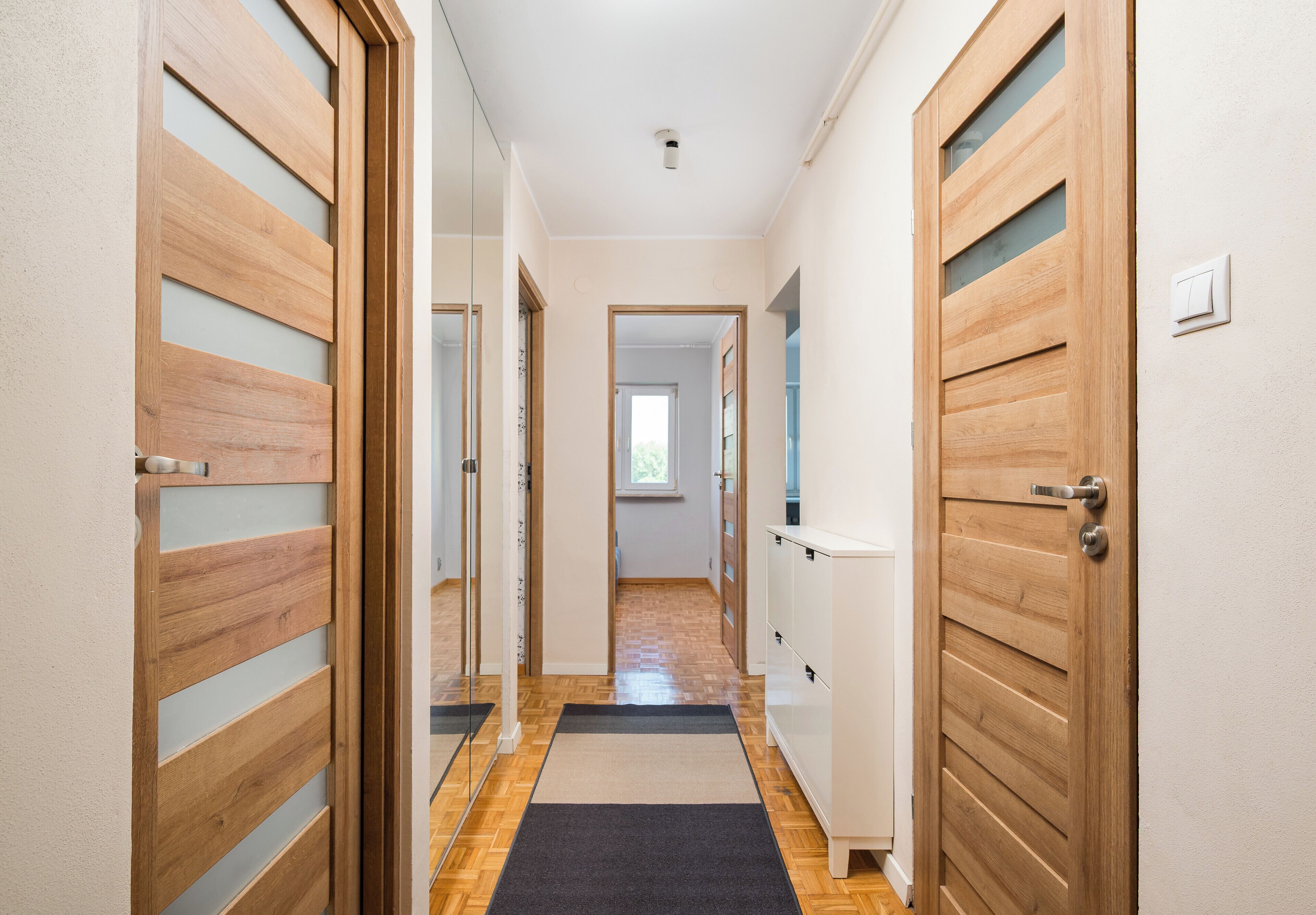 Un couloir avec des portes en bois, un radiateur et un interrupteur sur le mur.