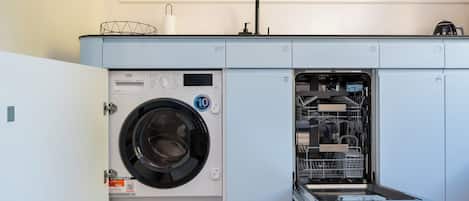 Une buanderie moderne et compacte, équipée d’un lave-linge à chargement frontal et d’un lave-vaisselle encastré.
