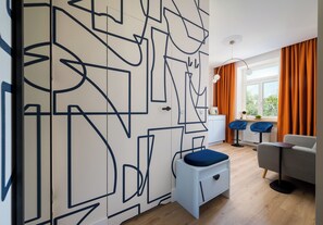 Una sala de estar moderna con un diseño geométrico en la pared, un sofá gris y un sillón azul.
