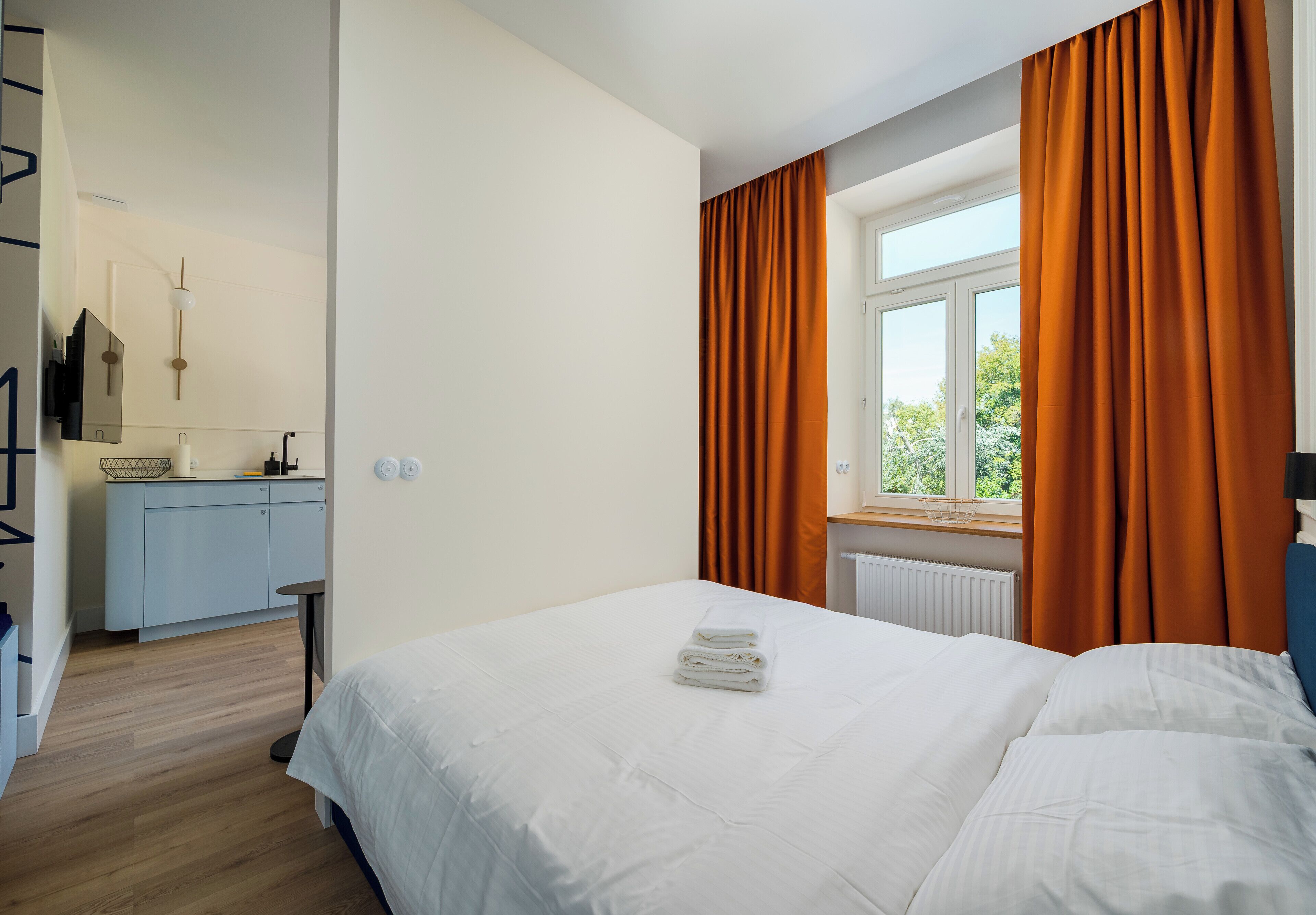 A hotel room with a bed, a window with curtains, a radiator, and a small table.
