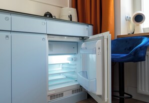 A modern kitchen with a built-in refrigerator, a coffee machine, and a blue chair. - Zachariasza Harmony Apartment (Warszawa)